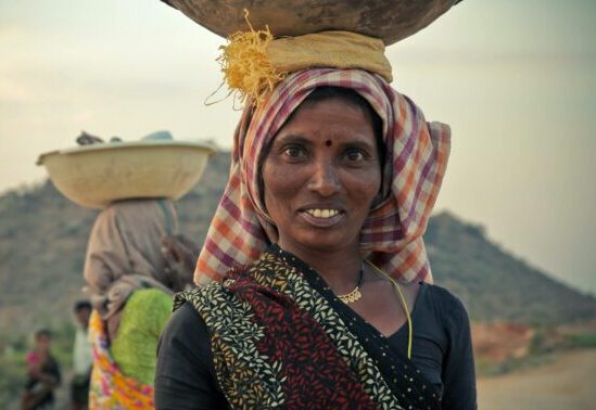 an Indian woman carries a heavy basket on her hear lengthening her neck beautifully